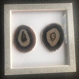 May include: Two agate slices framed in a white frame with a silver glitter border. The agate slices are brown and white with a natural pattern.