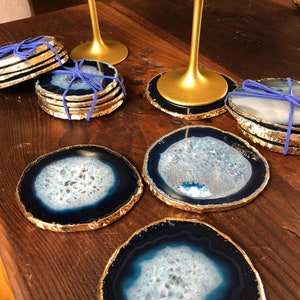 May include: Set of six blue agate coasters with gold trim. Each coaster features a unique natural pattern. The coasters are ideal for protecting surfaces from scratches and spills.