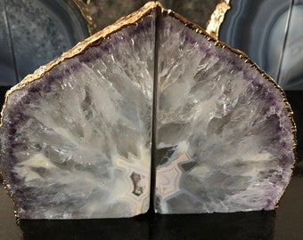 Puede incluir: Un par de sujetalibros hechos de rebanadas de ágata natural con ribete dorado. El ágata es de color púrpura claro y blanco con un patrón natural.