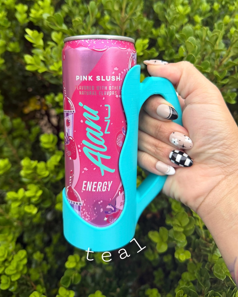 K&ouml;nnte beinhalten: Eine rosa Alani Nu Energy-Drink-Dose, die in einem t&uuml;rkisfarbenen Griff gehalten wird. Die Dose ist mit "Pink Slush" beschriftet und hat ein Erdbeer-Design. Der t&uuml;rkisfarbene Griff ist so konzipiert, dass er eng an die Dose passt.