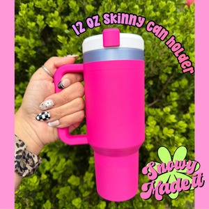 May include: A bright pink 12 oz skinny can holder with a white lid and handle. The can holder has the text "12 oz skinny can holder" and "Snowy Made It" in a playful font.