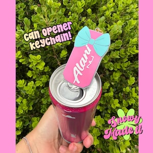 May include: A pink can opener keychain with a light blue bow design and the name "Alani" printed on it. The keychain is opening a pink can. The image also includes the text "can opener keychain!" and the logo "Snowy Made It".