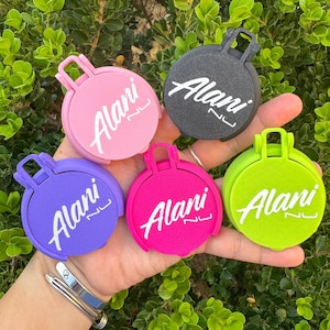 May include: A collection of five round, colorful items with a handle, each featuring the name "Alani" in white script. The items are in shades of pink, purple, black, green, and hot pink. A silver bracelet is visible in the lower left.