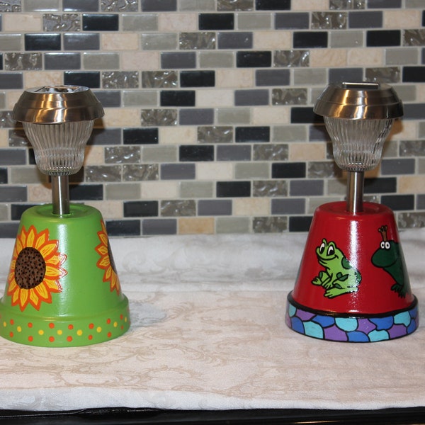 Solar lights with a hand painted 6" clay pot bases. Two designs sunflower or king toad and frog designs. Great to use in the kitchen or gift