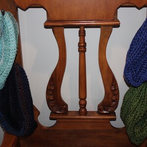 May include: Four knitted neck warmers hanging on hooks on a wooden chair. The neck warmers are in shades of blue, green, and teal.