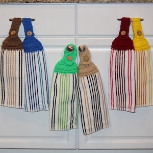 May include: Five crocheted kitchen towels with striped fabric and crocheted tops in various colors, including brown, blue, green, beige, red, and yellow. The towels are hanging on hooks.