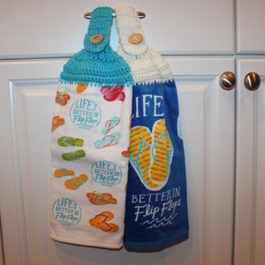 May include: Two crocheted dish towels hanging on a white cabinet door. The towels are blue and white with a pattern of flip flops and the text "Life's Better in Flip Flops".