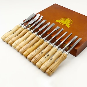 May include: A set of 12 wood carving tools with wooden handles and metal blades, arranged in a wooden box with a gold label that says "25 Years of Excellence".