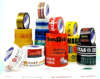 May include: Assortment of custom-made packing tape rolls with various logos and designs, including Toys R Us, Supreme, and Super Line. The tape rolls are arranged in a pile on a white surface.