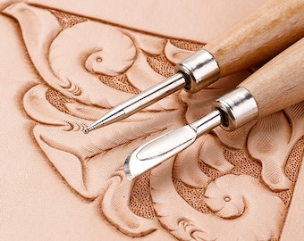 May include: Two leather carving tools with wooden handles. The tools are on a piece of leather that has been carved with a floral design.