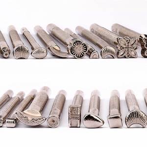 Pode incluir: Um conjunto de 20 ferramentas de estampagem de couro de metal prateado com vários desenhos, incluindo flores, borboletas e formas geométricas.