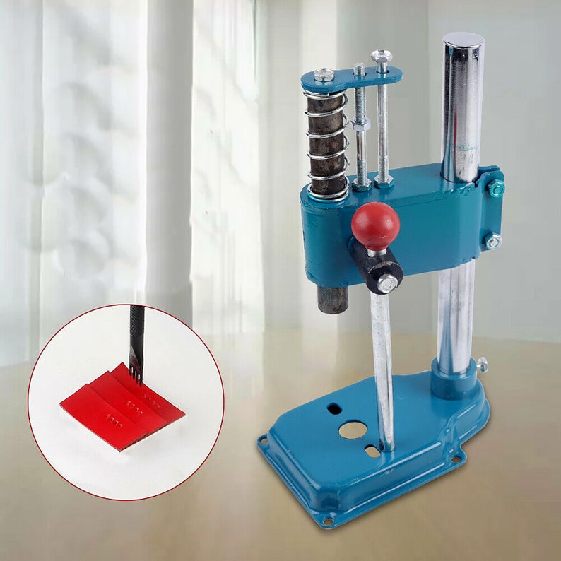 May include: A blue metal hand press with a silver lever and a red handle. The press has a spring-loaded mechanism and a base with a hole in the center. The press is used for pressing metal or other materials.