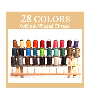 May include: A wooden thread rack with 28 spools of 0.45mm waxed thread in various colours. The rack has three tiers and is made of light brown wood.