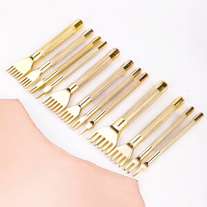 May include: A set of 10 gold leather stitching tools with different sized prongs. The tools are arranged in a row on a white surface.