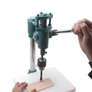 May include: A green leather punch tool with a handle and a white base. The tool is being used to punch holes in a piece of brown leather.