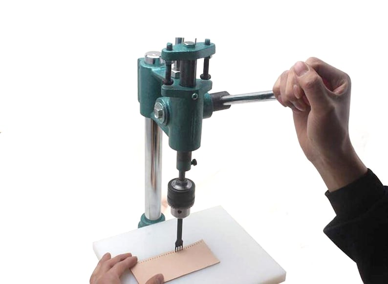 May include: A green leather punch tool with a handle and a white base. The tool is being used to punch holes in a piece of brown leather.