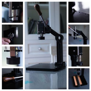 May include: A black metal press with a wooden handle and a black base. The press is used for making leather goods.
