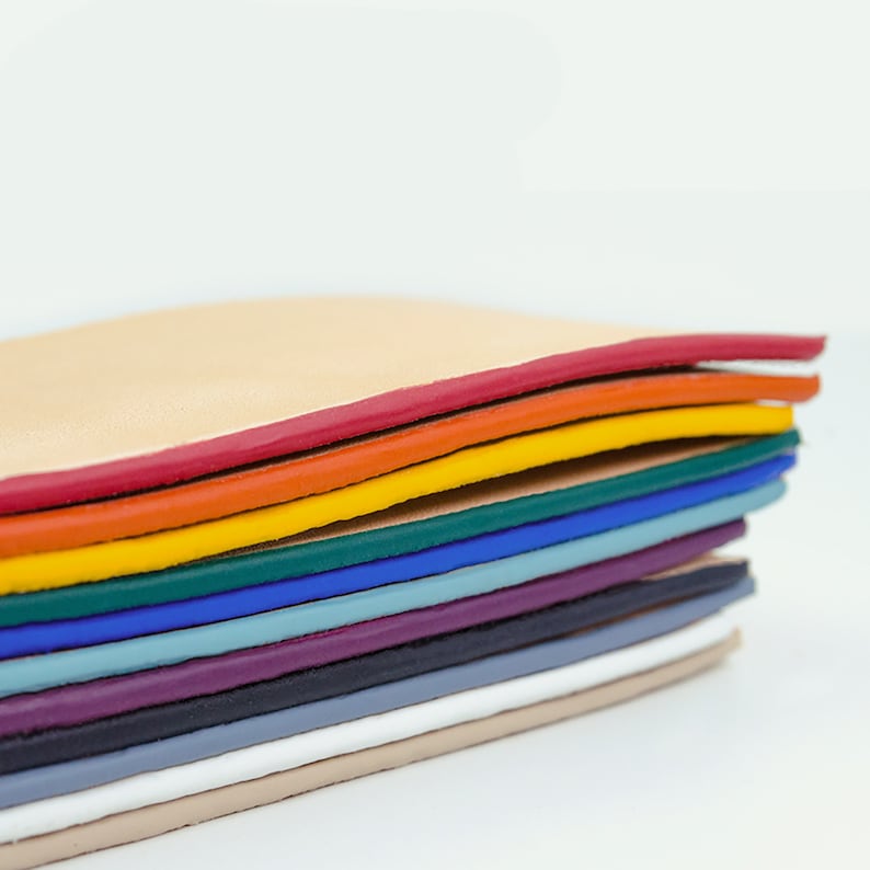 Op de afbeelding: Een stapel kleurrijke lederen stukken, elk met een rand in een andere kleur. De kleuren zijn rood, oranje, geel, groen, blauw, lichtblauw, paars, grijs, wit en beige.