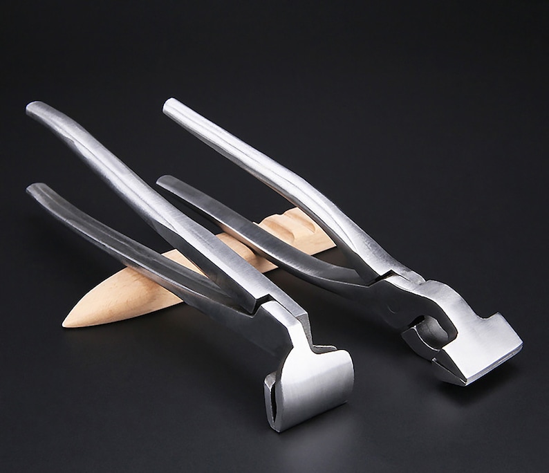 May include: Two silver metal pliers with a flat, rectangular jaw. The pliers are on a wooden surface.