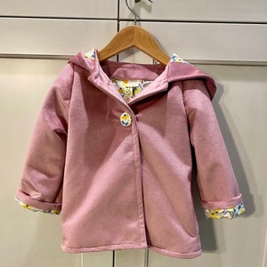 May include: A pink hooded jacket with a floral print lining. The jacket has a single button closure and long sleeves.