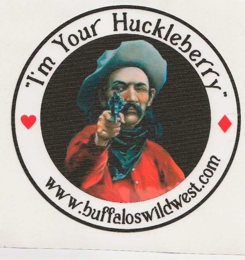 May include: A black and white circular sticker with a cowboy holding a gun and pointing it at the viewer. The sticker has the text "I'm Your Huckleberry" and "www.buffaloswildwest.com" around the edge.