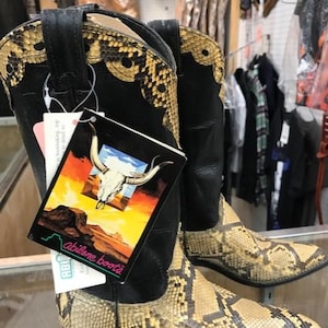 May include: A pair of black leather cowboy boots with a snakeskin pattern. The boots have a pointed toe and a high heel. The boots are labeled "Abilene Boots".