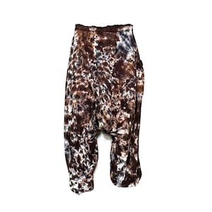 Pode incluir: Calças marrons e brancas com estampa tie-dye, de corte solto e fluido. As calças têm uma cintura larga e um bolso no lado direito.