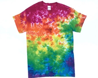 Könnte beinhalten: Ein Batik-T-Shirt mit einem Regenbogenmuster in den Farben Pink, Orange, Gelb, Grün, Blau und Lila.