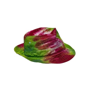 May include: A bucket hat featuring a vibrant tie-dye pattern in shades of bright pink, lime green, and white. The hat has a rounded crown and a downward-sloping brim with visible stitching details throughout the fabric construction.