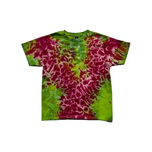 May include: A short-sleeve crew neck t-shirt featuring a vibrant tie-dye pattern in shades of bright magenta, lime green, and olive green. The design displays a concentrated V-shaped pattern of magenta radiating from the center against a green background.