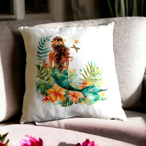 May include: A white throw pillow with a watercolor illustration of a mermaid with green and blue tail, surrounded by tropical plants and flowers. The mermaid is wearing a flower crown.