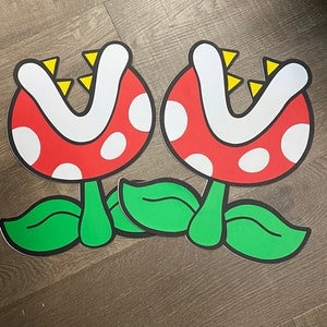 May include: Two red and white plant-like decorations with green leaves. The decorations have a large, open mouth with yellow teeth.