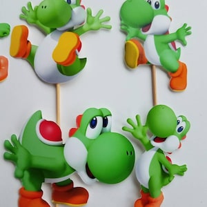 May include: Four green Yoshi cake toppers with different poses. Each topper is made of cardboard and has a stick attached to the back.
