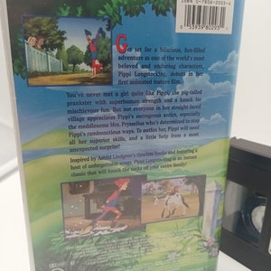K&ouml;nnte beinhalten: Eine VHS-Kassette des Zeichentrickfilms "Pippi Langstrumpf" in einer Plastikverpackung. Die R&uuml;ckseite des Geh&auml;uses zeigt farbenfrohe Illustrationen von Pippi und Text, der die Handlung und die Charaktere des Films beschreibt. Das Band ist ein klassischer Zeichentrickfilm.