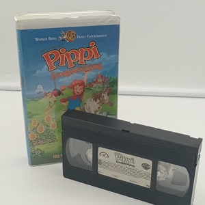 K&ouml;nnte beinhalten: Eine VHS-Kassette und ihre H&uuml;lle f&uuml;r den Zeichentrickfilm "Pippi Langstrumpf". Das Geh&auml;use hat einen blauen Himmelshintergrund mit Zeichentrickfiguren und dem Warner Bros.-Logo. Die schwarze VHS-Kassette befindet sich neben dem Geh&auml;use.