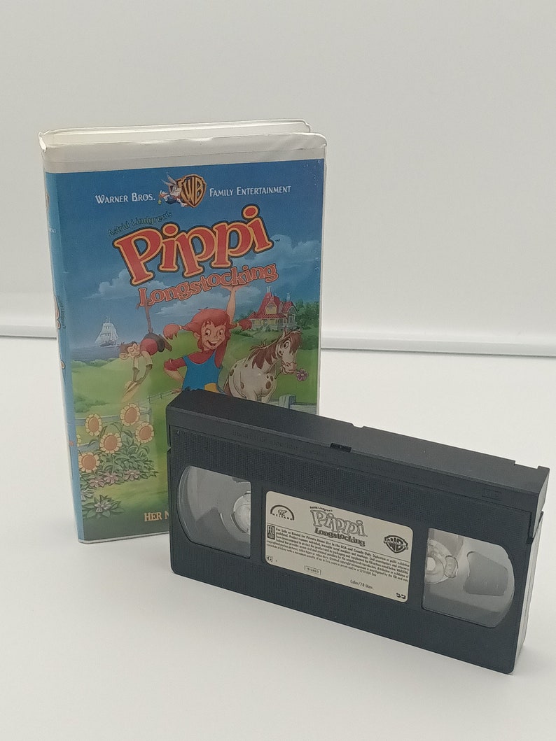 K&ouml;nnte beinhalten: Eine VHS-Kassette und ihre H&uuml;lle f&uuml;r den Zeichentrickfilm "Pippi Langstrumpf". Das Geh&auml;use hat einen blauen Himmelshintergrund mit Zeichentrickfiguren und dem Warner Bros.-Logo. Die schwarze VHS-Kassette befindet sich neben dem Geh&auml;use.