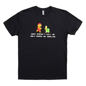 Peut inclure: T-shirt noir avec une image pixelisée de Mario et d'une tortue, et le texte "Ce qui ne me tue pas me rend plus petit."