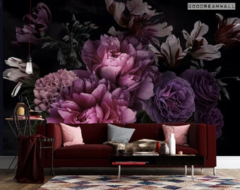Könnte beinhalten: Ein dunkelrotes Samtsofa mit einer floralen Tapete mit großen rosa und violetten Blumen. Das Sofa hat drei Kissen, zwei sind rosa und eines ist grau. Das Sofa steht vor einer schwarzen Wand.