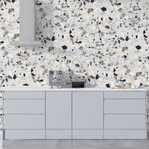 May include: A kitchen with gray cabinets and a white countertop. The backsplash is a terrazzo pattern with white, gray, and brown flecks. A stainless steel espresso machine sits on the countertop.