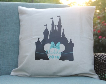May include: A white pillow with a black silhouette of Cinderella's castle and a turquoise glitter Mickey Mouse head with the text "Disney 2018".