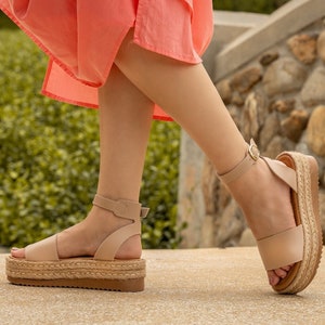 May include: A pair of beige platform sandals with ankle straps. The sandals have a woven jute platform and a leather upper.