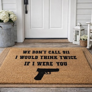 May include: A rectangular doormat with a brown coir surface and a woven border. The mat features the text "WE DON'T CALL 911 I WOULD THINK TWICE IF I WERE YOU" and a black handgun silhouette.