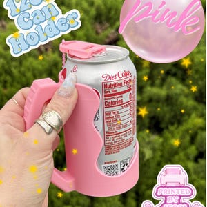 May include: A light pink 12oz can holder with a handle and a small top tab, holding a silver Diet Coke can. The text 12oz Can Holder, Pink, and Printed By Jessi appears in the image. The holder features a contoured grip and a chain attachment.