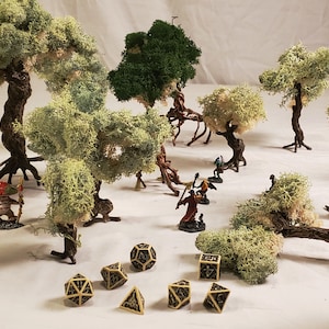 May include: A tabletop scene with miniature figures and dice, surrounded by artificial moss trees. The scene features a variety of trees, including a large green tree, a smaller green tree, and several white moss trees. The miniature figures are painted in various colors and are standing on a brown surface. The dice are black and white and are scattered around the figures.