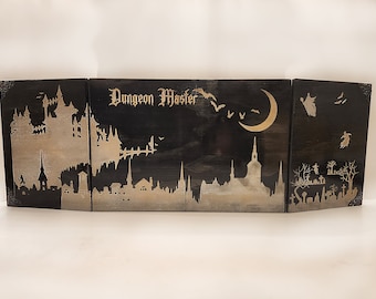 Może przedstawiać: Trójpanelowy drewniany ekran Dungeon Master z czarnym tłem i złotymi sylwetkami miejskiego horyzontu, nietoperzy, rosnącego księżyca i cmentarza. Panel środkowy zawiera napis "Dungeon Master" złotymi literami.