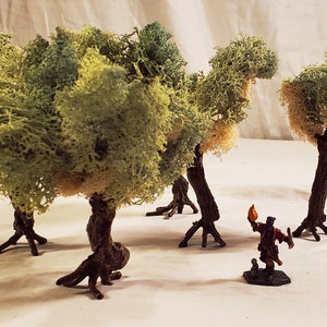 May include: Four miniature trees made of green and brown moss with a small figurine of a person holding a torch standing in front of them.