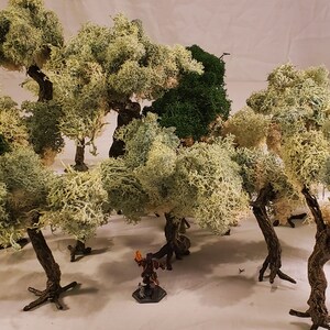 May include: A collection of miniature trees made of white and green moss, with a small figure standing in the center. The trees are arranged in a cluster, creating a miniature forest scene.