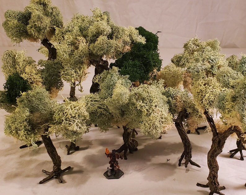 May include: A collection of miniature trees made of white and green moss, with a small figure standing in the center. The trees are arranged in a cluster, creating a miniature forest scene.
