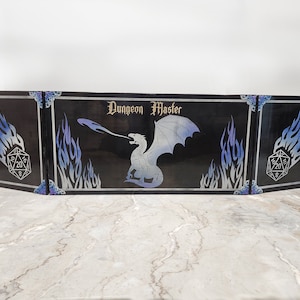 Może przedstawiać: Czarny drewniany ekran Dungeon Master z białym wzorem smoka i niebieskimi płomieniami. Ekran składa się z trzech paneli i na każdym panelu bocznym znajduje się 20-ścienna kostka.