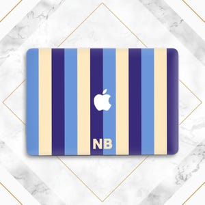 May include: A rectangular laptop skin featuring a vertical striped pattern in alternating shades of light blue, dark navy blue, and cream. The center displays a white Apple logo above the capital letters NB printed in a bold, sans-serif font.